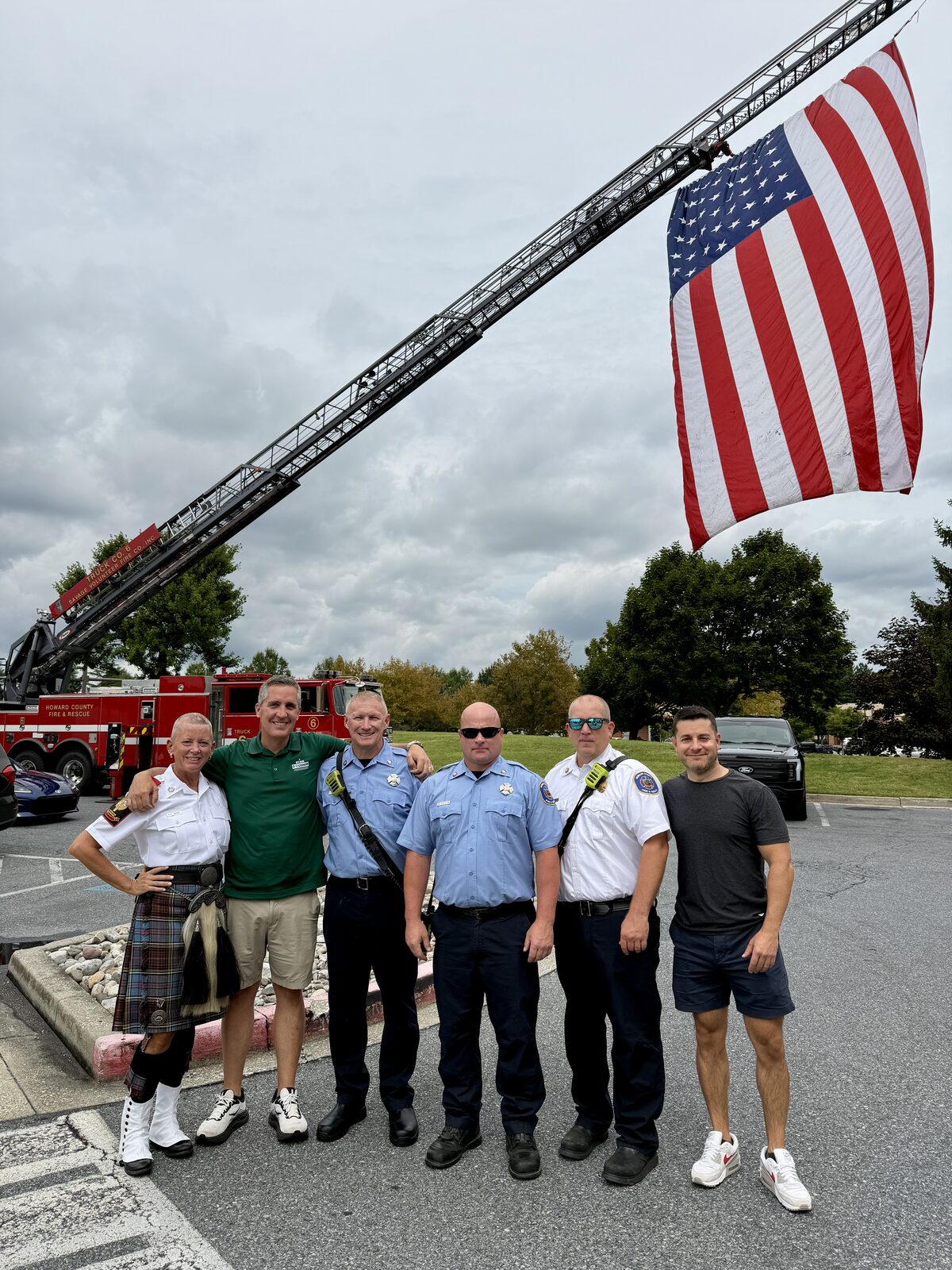 Ryan O’Connor with Howard County firefighters and Eric Hoover beneath an American flag hung from a Howard County Fire and Rescue ladder truck